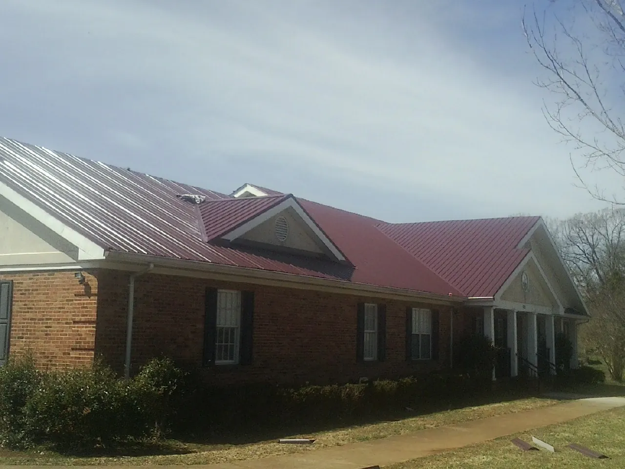 Red metal roof with gabled entries on a long brick building, from a Hail Damage Roof Repair job in Church Road