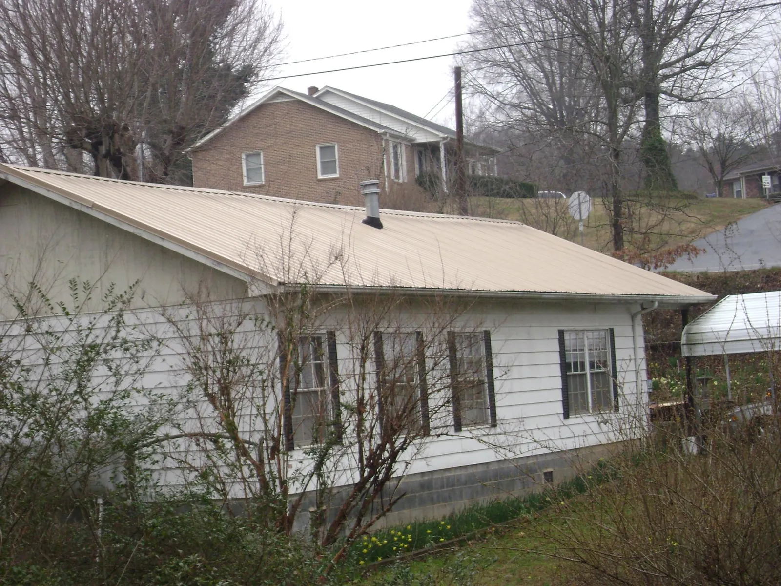 Tan metal roof on a white sided house set into a hillside — Commercial Roofing by Roofing Brothers in Church Road